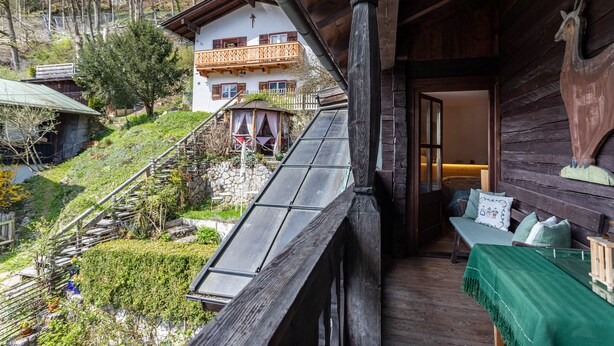 A wooden cabin with a balcony, a bed with a green bedspread, and a view of a house with a balcony.
