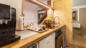 A modern kitchen with a coffee machine, wooden countertop, and a view of a wooden staircase.