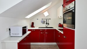 A kitchen with red cabinets, a microwave, a sink, and a window. - Holiday Apartment "Domicilio Azzurro" with Lake View and Wi-Fi (Lindau am Bodensee)
