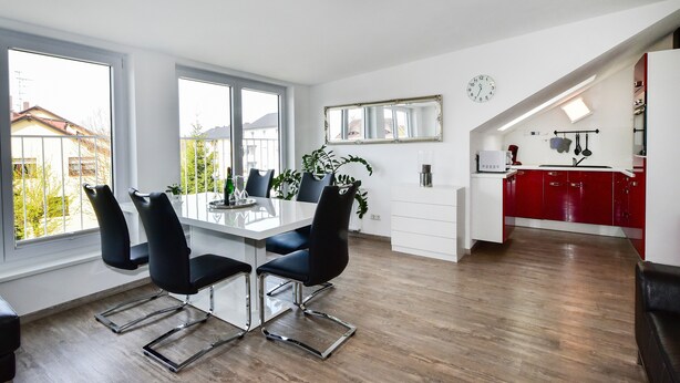 A modern kitchen with red cabinets, a white countertop, and a dining area with a white table and black chairs. - Holiday Apartment "Domicilio Azzurro" with Lake View and Wi-Fi (Lindau am Bodensee)