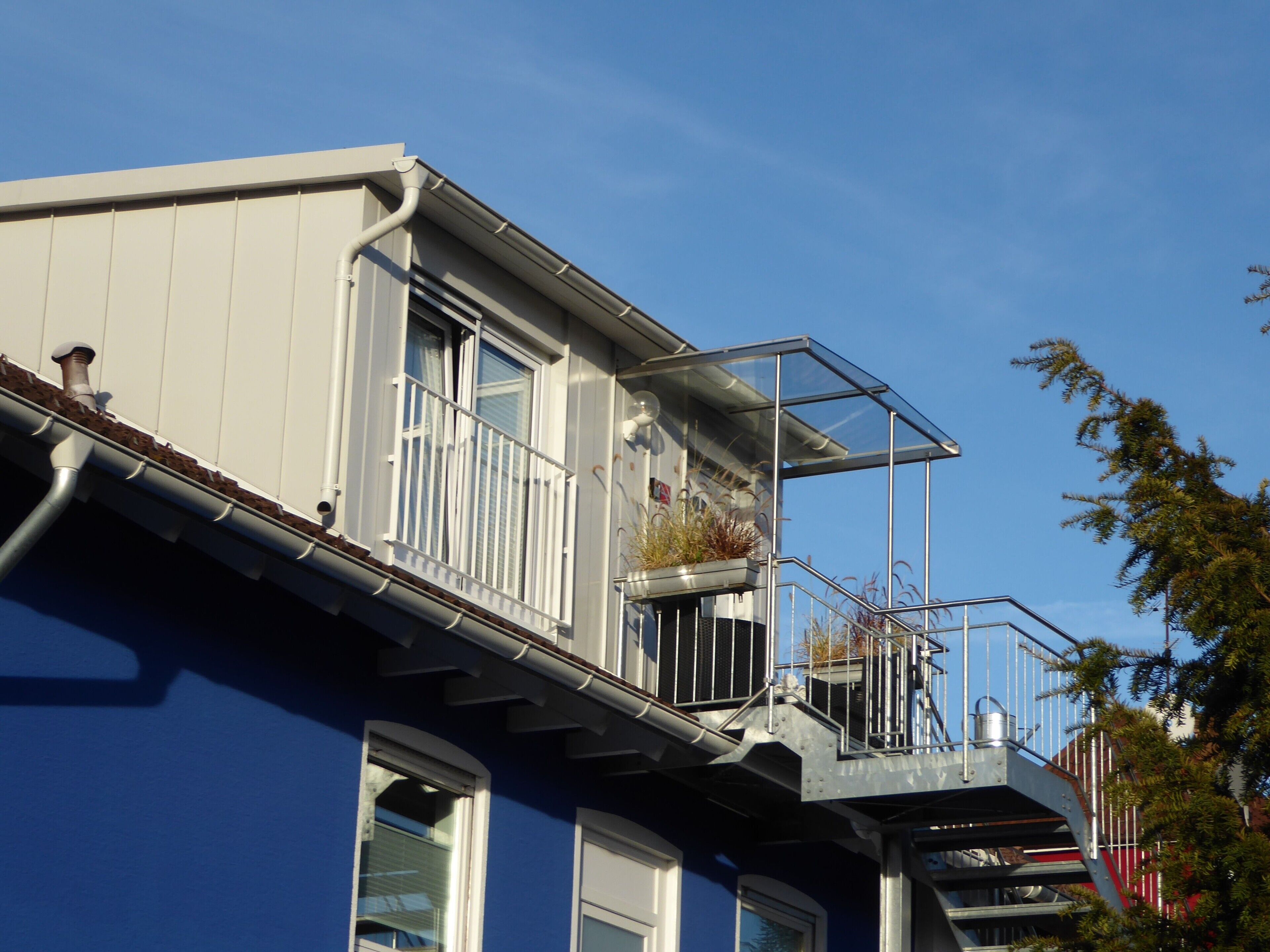 Een woongebouw met een blauwe gevel, een balkon met planten en een zichtbare trap.