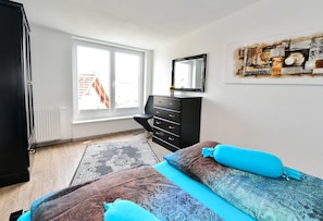 A bedroom with a bed, dresser, window, and artwork on the wall.
