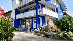 A two-story building with balconies, a stone pathway, and a garden with rocks and plants. - Holiday Apartment "Domicilio Azzurro" with Lake View and Wi-Fi (Lindau am Bodensee)