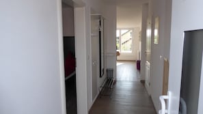 Kapea käytävä, jossa on naulakko, metallinen hylly ja ovi, joka johtaa huoneeseen.