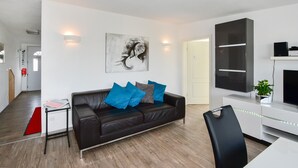 A modern living room with a black leather sofa, a flat-screen TV, and a minimalist design. - Holiday Apartment "Domicilio Azzurro" with Lake View and Wi-Fi (Lindau am Bodensee)