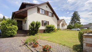 A two-story house with a sloped roof, a front entrance with steps, and a paved driveway. - Holiday Apartment "Sonnenbühl" with Lake View, Private Balcony and Wi-Fi (Aulendorf)