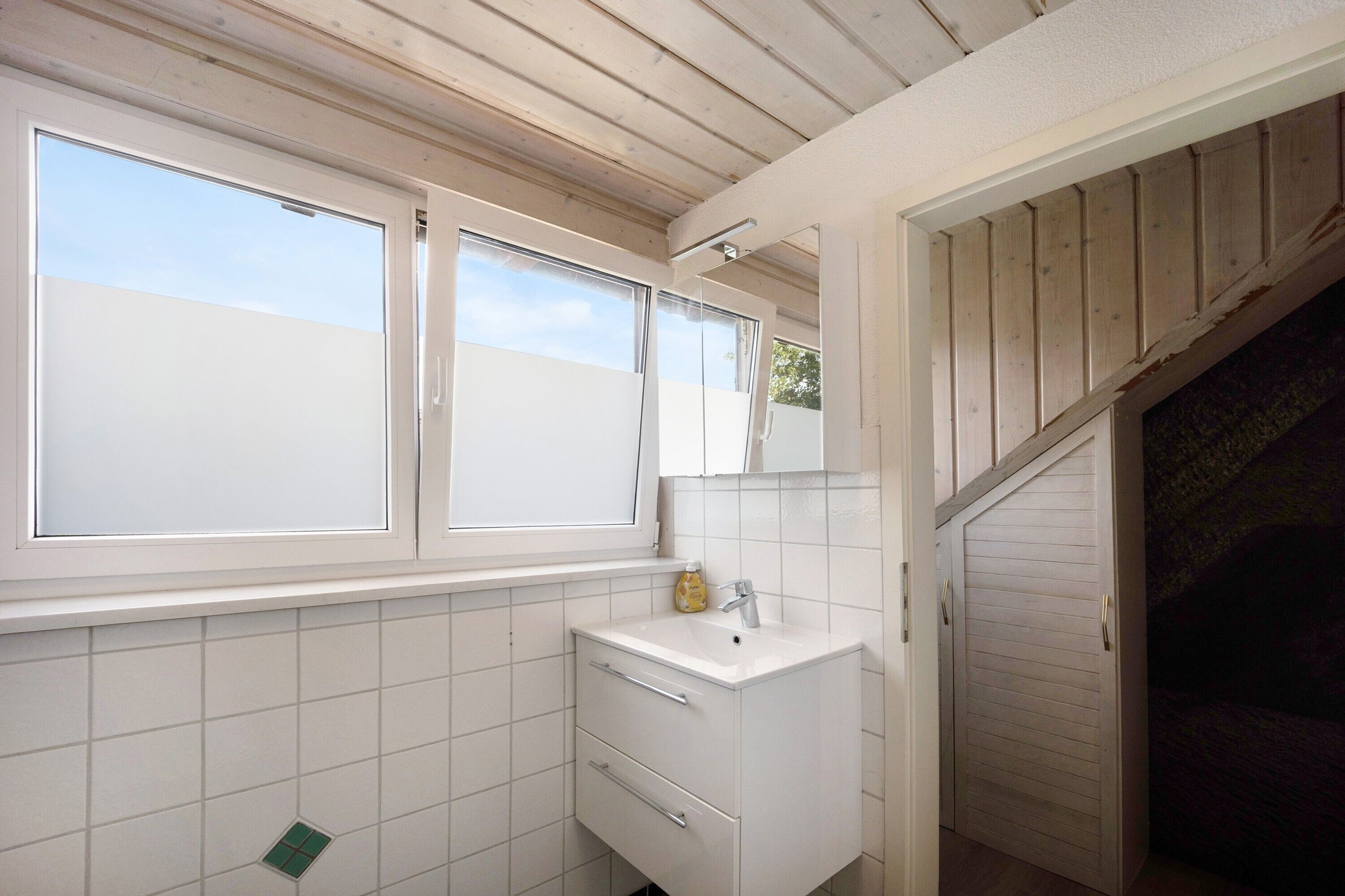 Ein Badezimmer mit einem weißen Waschbecken, zwei Schubladen, einem Spiegel und einem Fenster.