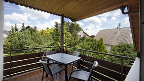 A covered outdoor balcony with a table and chairs, overlooking a residential area with trees and houses. - Holiday Apartment "Sonnenbühl" with Lake View, Private Balcony and Wi-Fi (Aulendorf)