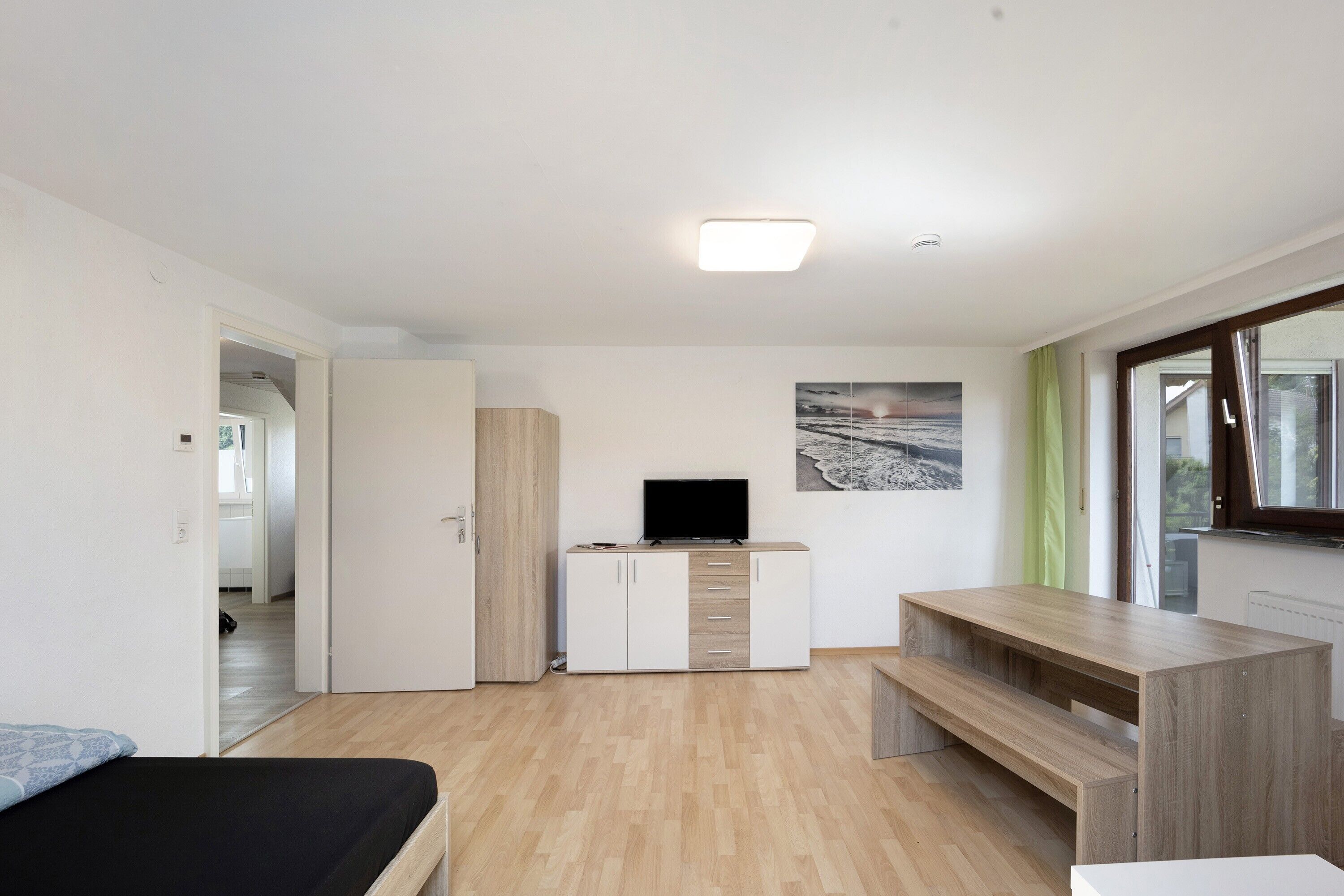 Ein modernes Zimmer mit einem Bett, einem Fernseher auf einer Kommode, einer Holzbank und einem Fenster.