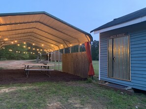 Ett takförsett utomhusområde med ett picknickbord och ljusslingor, intill en byggnad som är märkt med texten "Badhus".