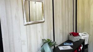 Huoneessa on puinen seinä, musta konsolipöytä, valkoinen seinälle kiinnitetty peili, koristeellinen ankkuri ja ruukussa oleva kasvi.