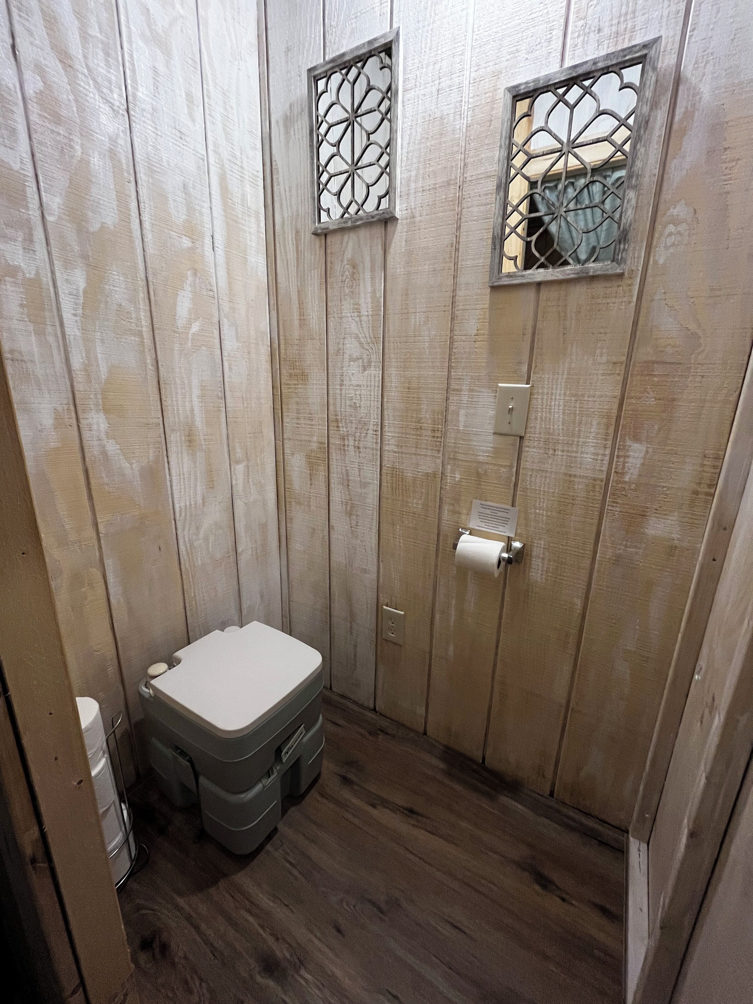 A small, wooden-paneled bathroom with a toilet, a sink, and a shower stall.