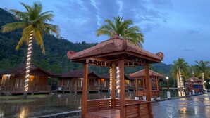 Une structure en bois dotée d’un toit et d’un banc, entourée d’eau et de palmiers.