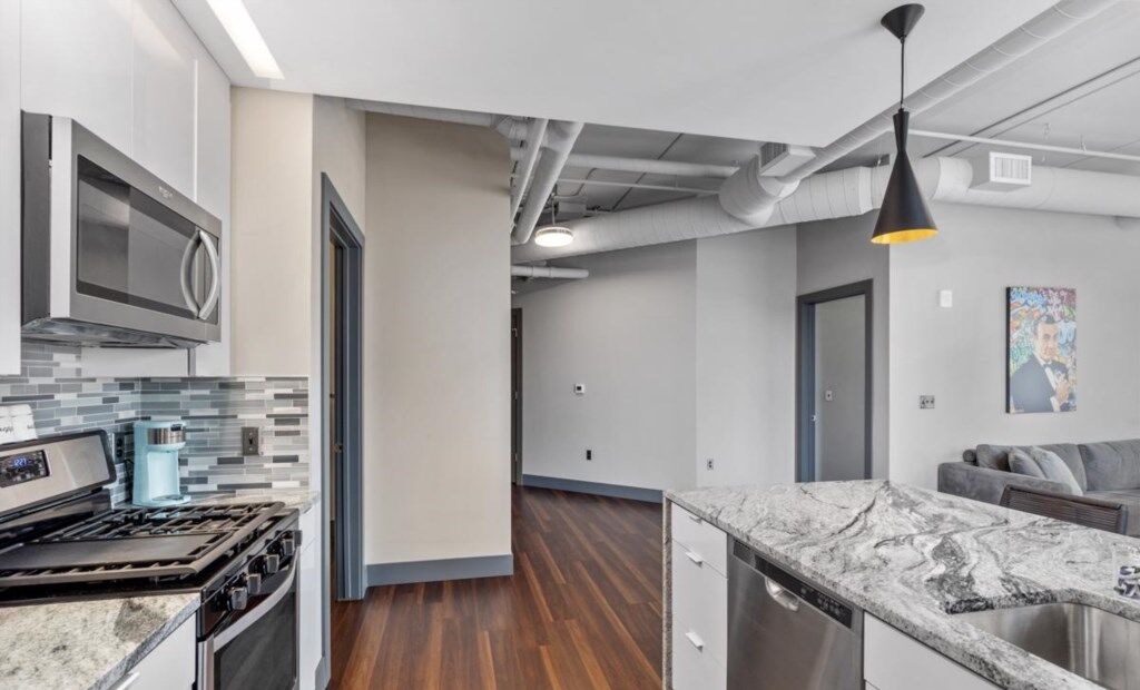 A modern kitchen with a built-in microwave, stove, and dishwasher, a wooden floor, and a gray and white color scheme.