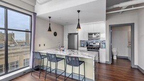Cocina moderna con isla de mármol, lámparas colgantes negras y vistas de la ciudad a través de amplios ventanales.