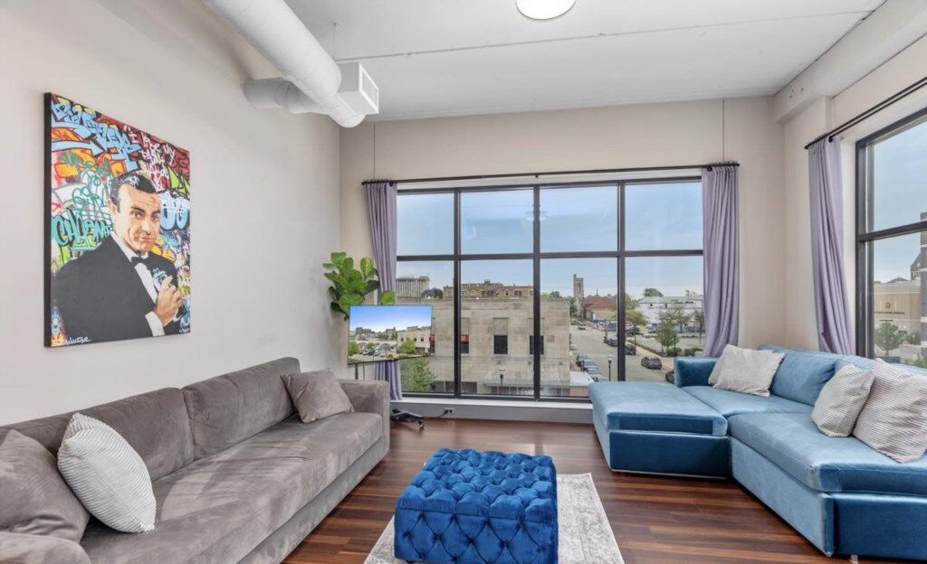 Una sala de estar moderna con un sofá gris, un sofá modular azul y un ventanal con vistas a la ciudad.