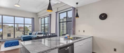 A modern kitchen with a large island, built-in dishwasher, and pendant lighting.