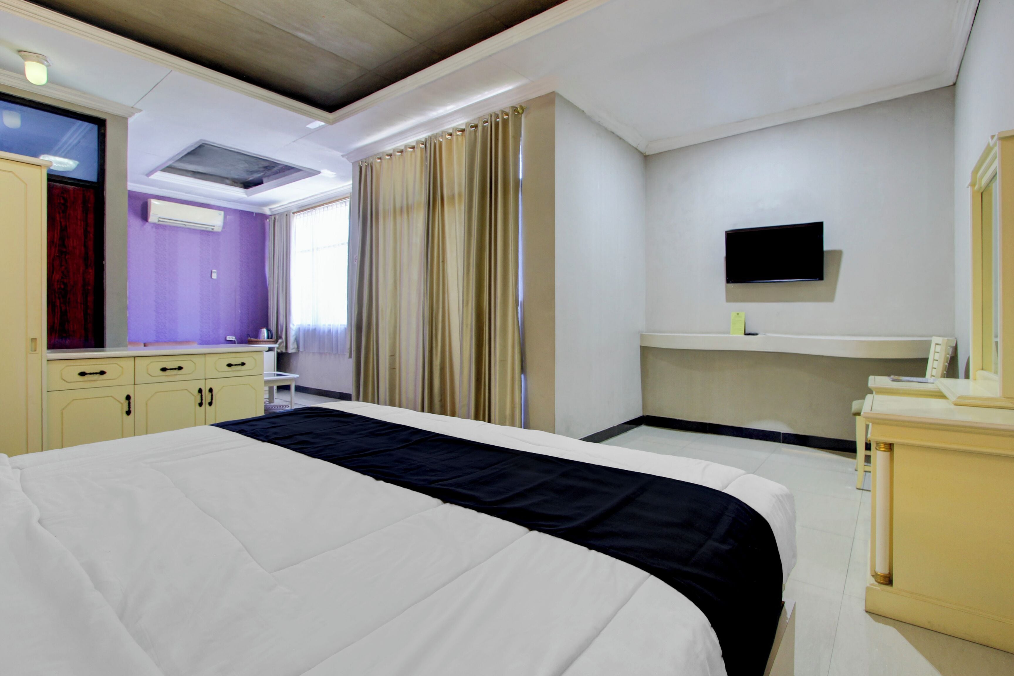 A hotel room with a bed, a desk, a television, and a window with curtains.