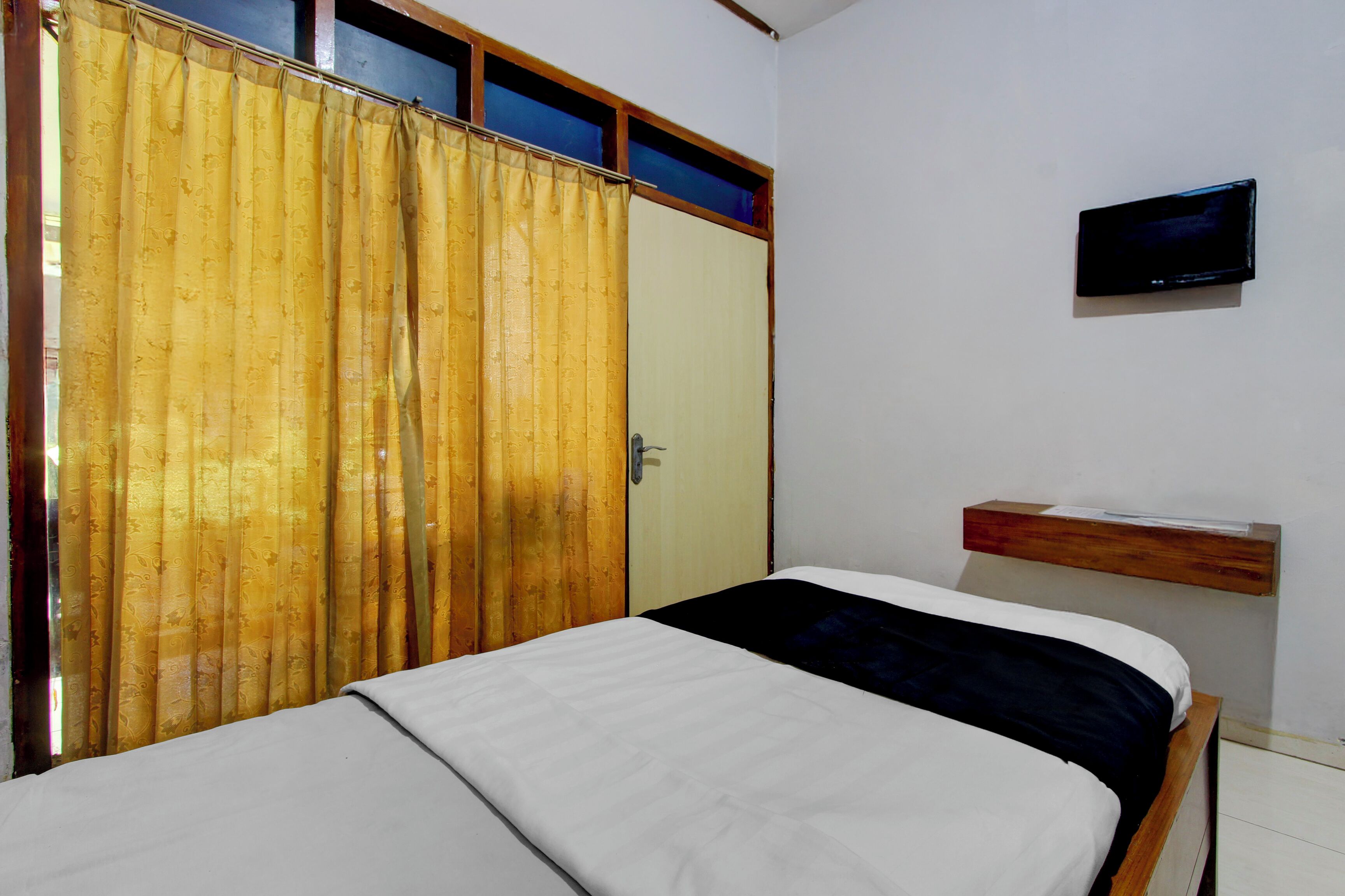 Une chambre à coucher avec un lit, un téléviseur fixé au mur et une fenêtre avec des rideaux.