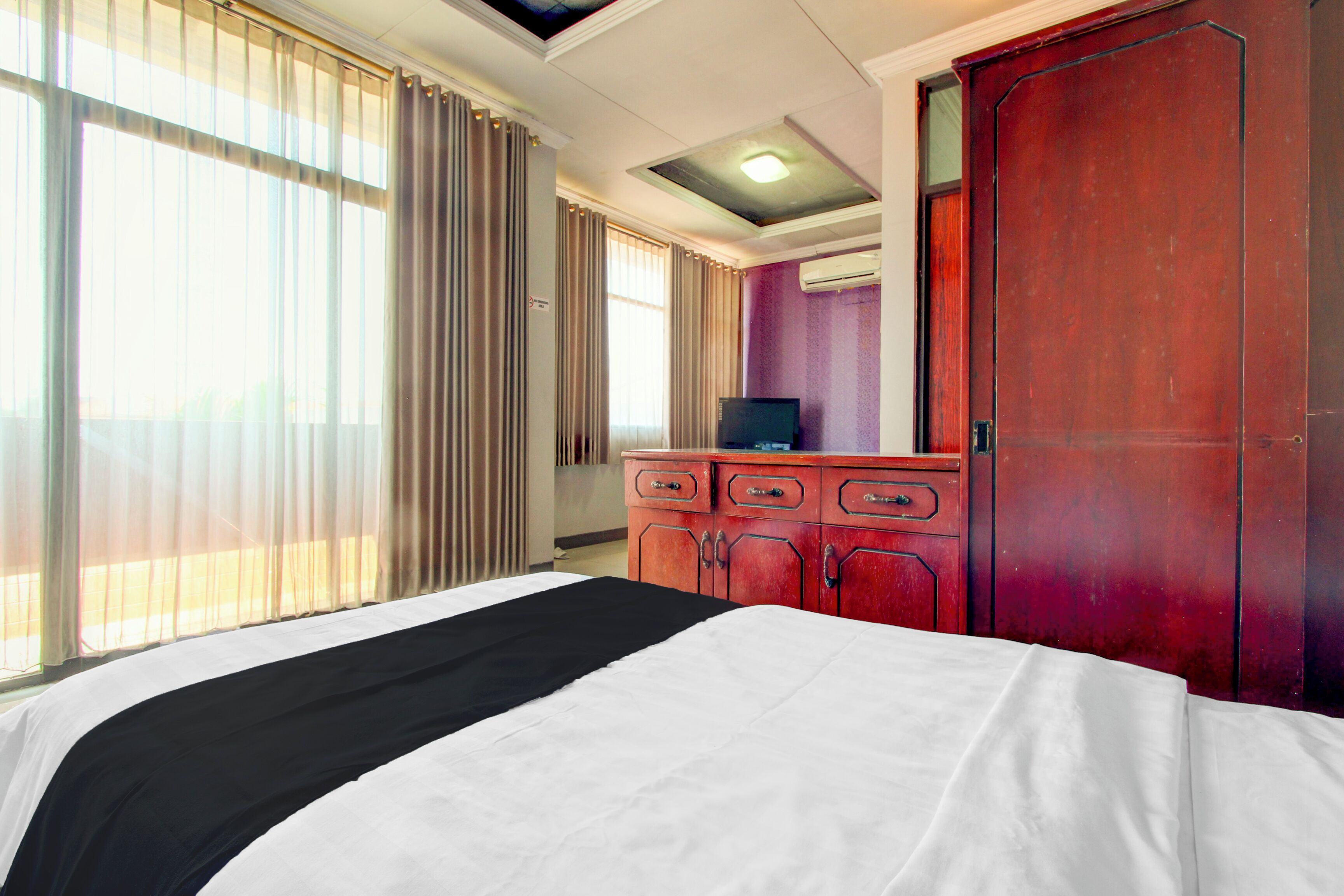 A hotel room with a bed, a dresser, a television, and a window with curtains.