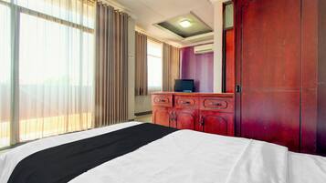 A hotel room with a bed, a dresser, a television, and a window with curtains.