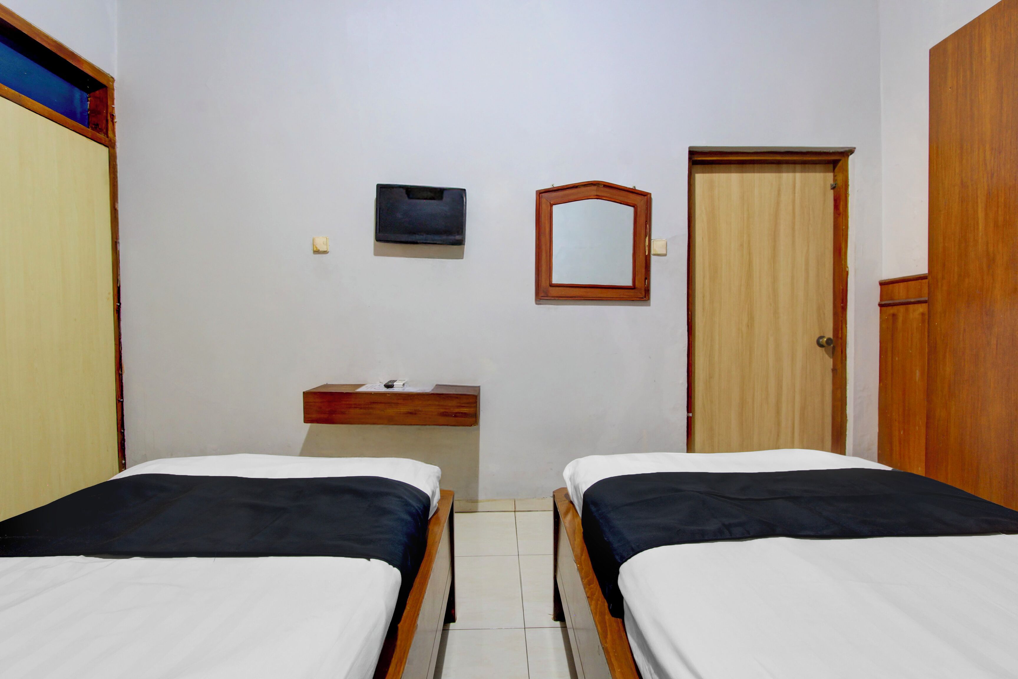 Una habitación con dos camas individuales, un armario de madera, una cómoda de madera, un espejo y un estante pequeño.