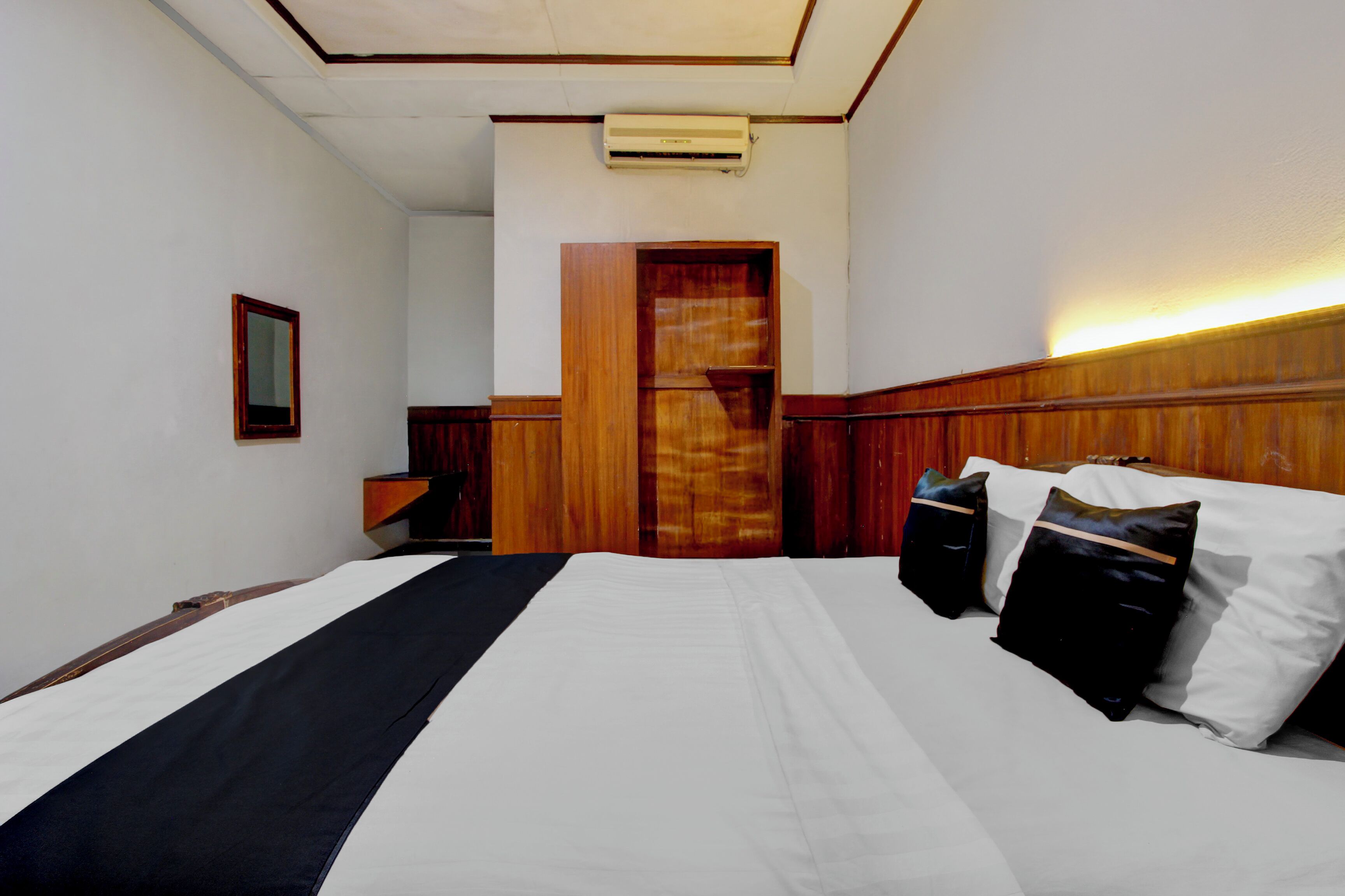 A hotel room with a bed, bedside tables, a mirror, and a wooden wardrobe.