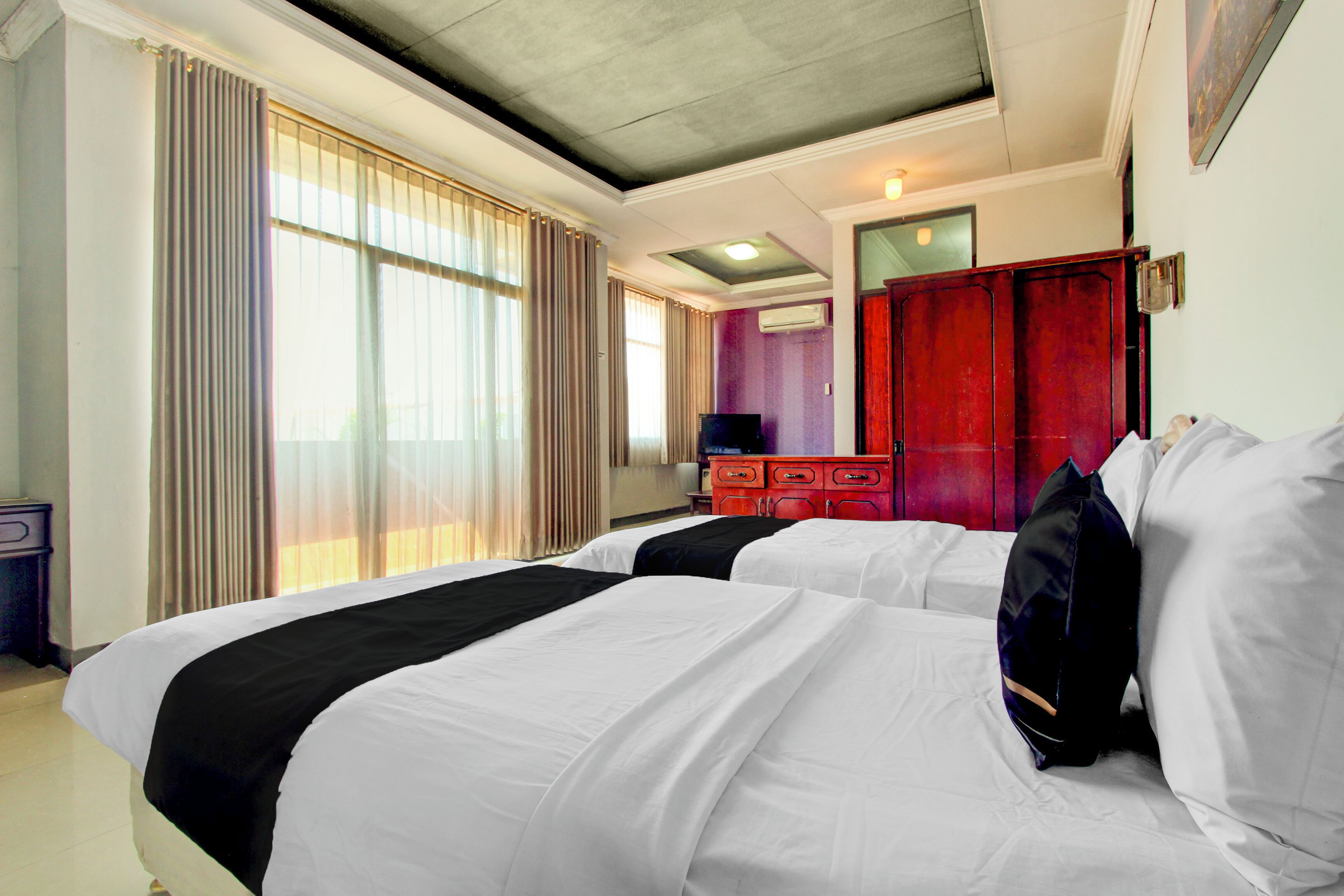 A hotel room with two beds, a TV, a wardrobe, and a large window with curtains.