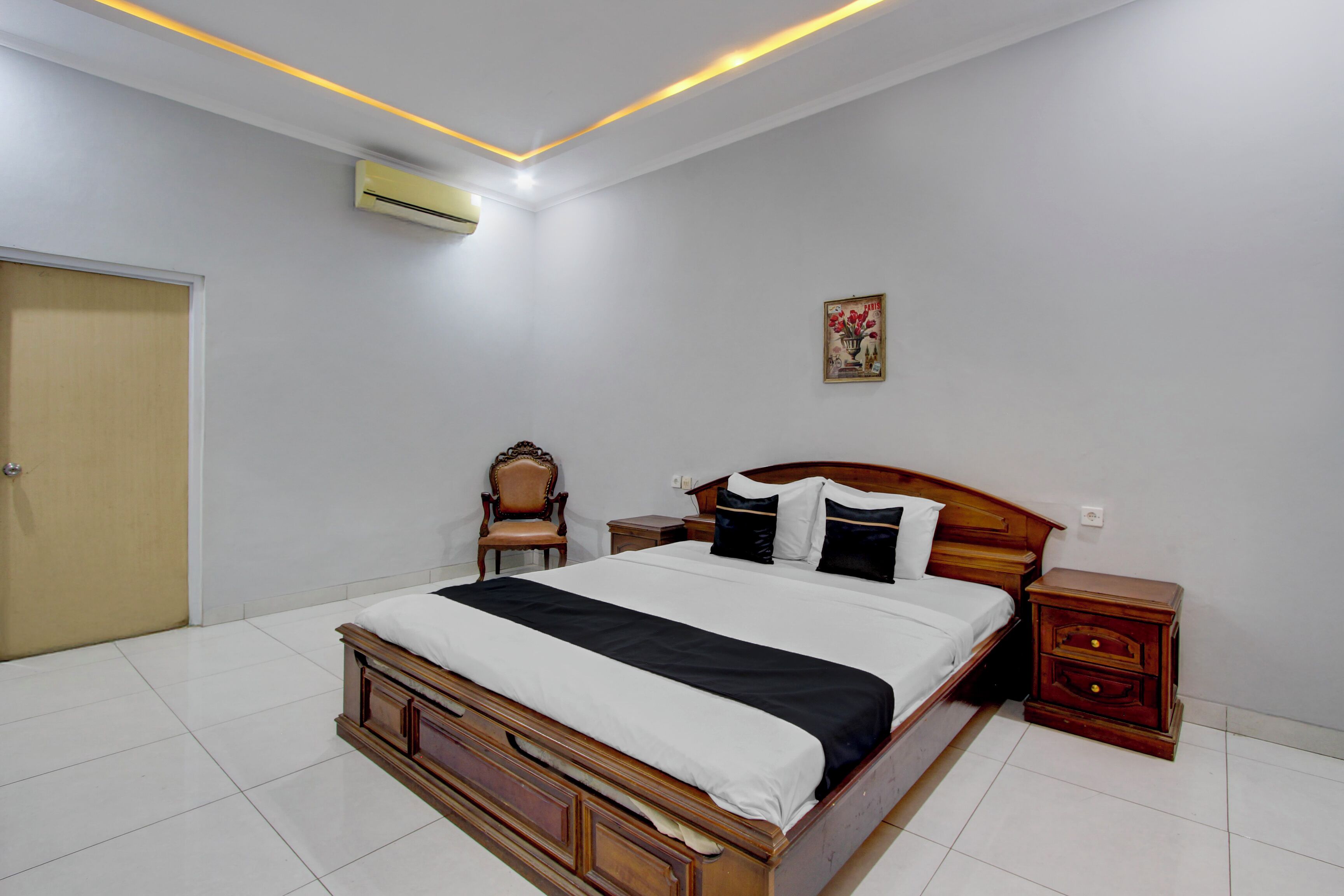 A bedroom with a wooden bed, a nightstand, a chair, a door, and a wall-mounted air conditioner.