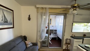 Een knus woongedeelte met een bank, een eettafel, een keukenhoek en een schuifdeur naar een buitenbalkon.