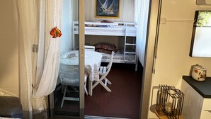 Een kamer met een stapelbed, een klein tafeltje met een stoel, een raam met gordijnen en een aan de muur bevestigde televisie.