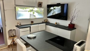 Een moderne keuken met een zwart aanrecht, witte kasten, een ingebouwde kookplaat en een flatscreen televisie die boven het aanrecht is bevestigd.