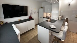 Een moderne keuken met een flatscreen televisie, een klein eilandje met zitplaatsen, witte kasten en een betegelde spatwand.
