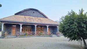 A building with a tiled roof, a covered porch with wooden railings, and a stone foundation. - LAKE NYASA RESORT & CAMPSITE  (Matema)