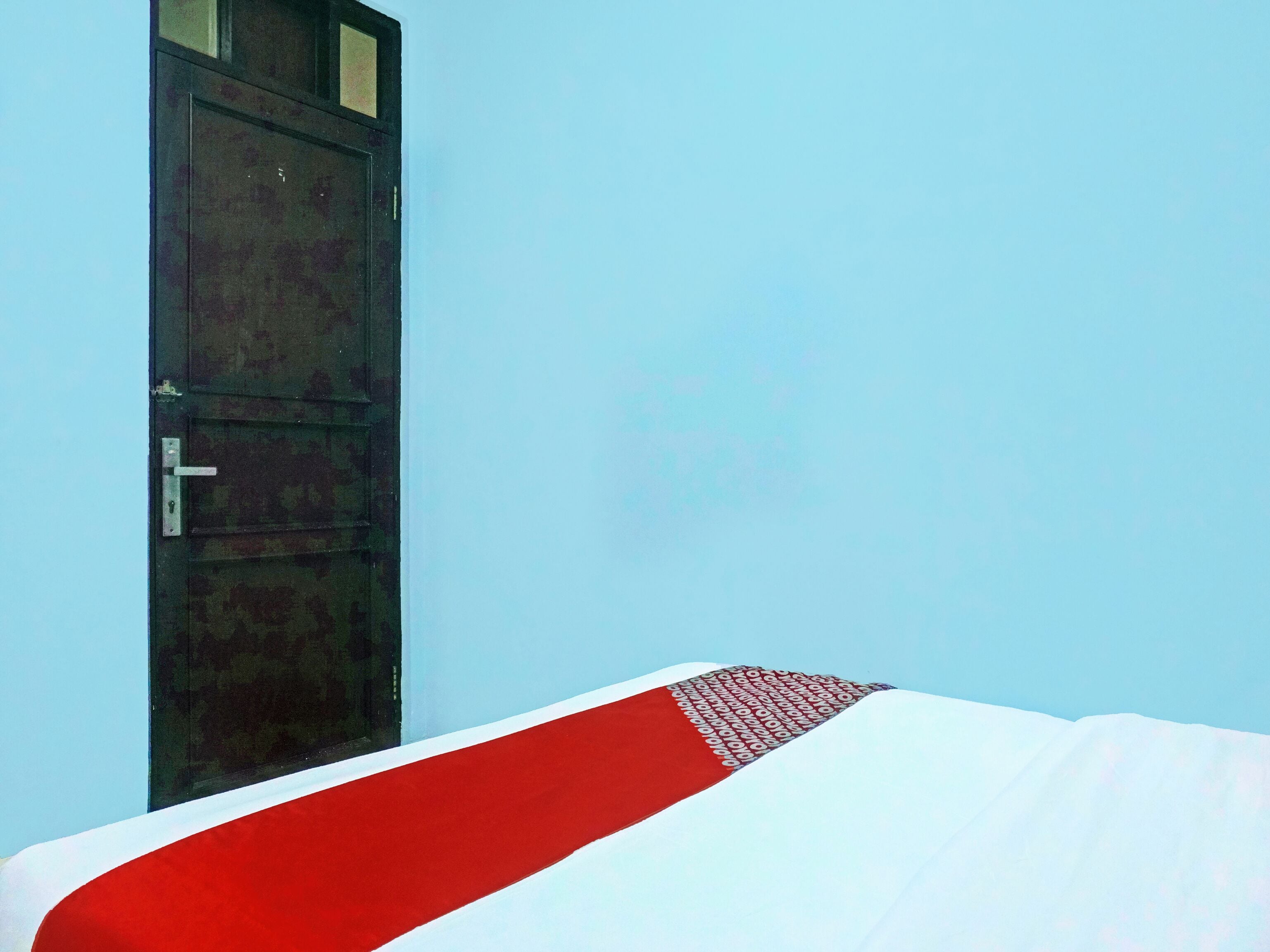 A room with a bed, a wooden door, and a light blue wall.