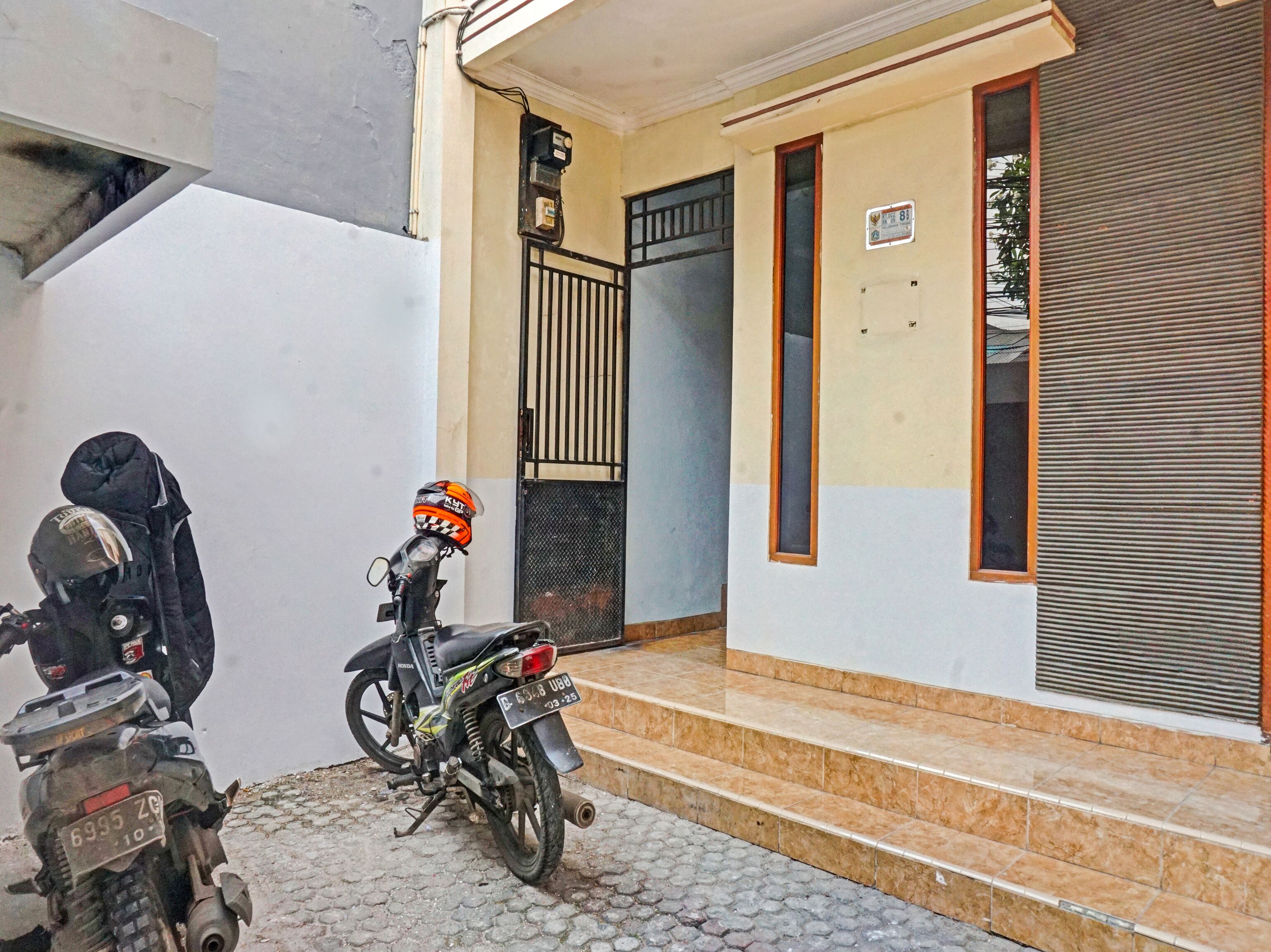 Una motocicleta estacionada en un camino de adoquines frente a un edificio con entrada de azulejos y una puerta de metal.