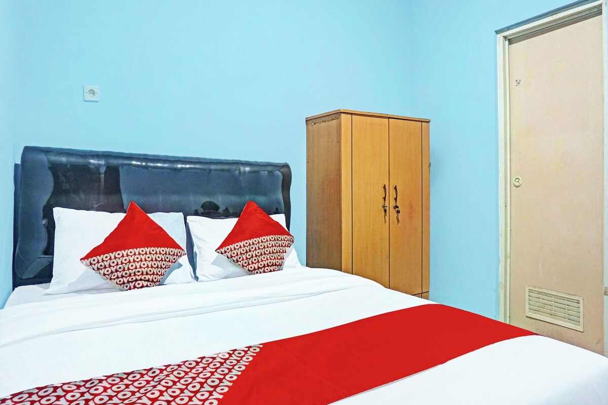 A bed with a blue headboard, two red pillows, and a white bedspread with a red and white pattern.