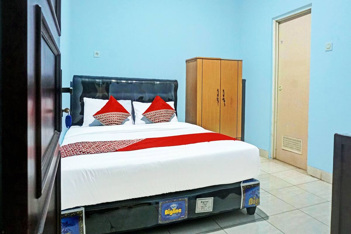 A neatly made bed with a white and red bedspread, two red pillows, and a wooden wardrobe in a room with light blue walls.
