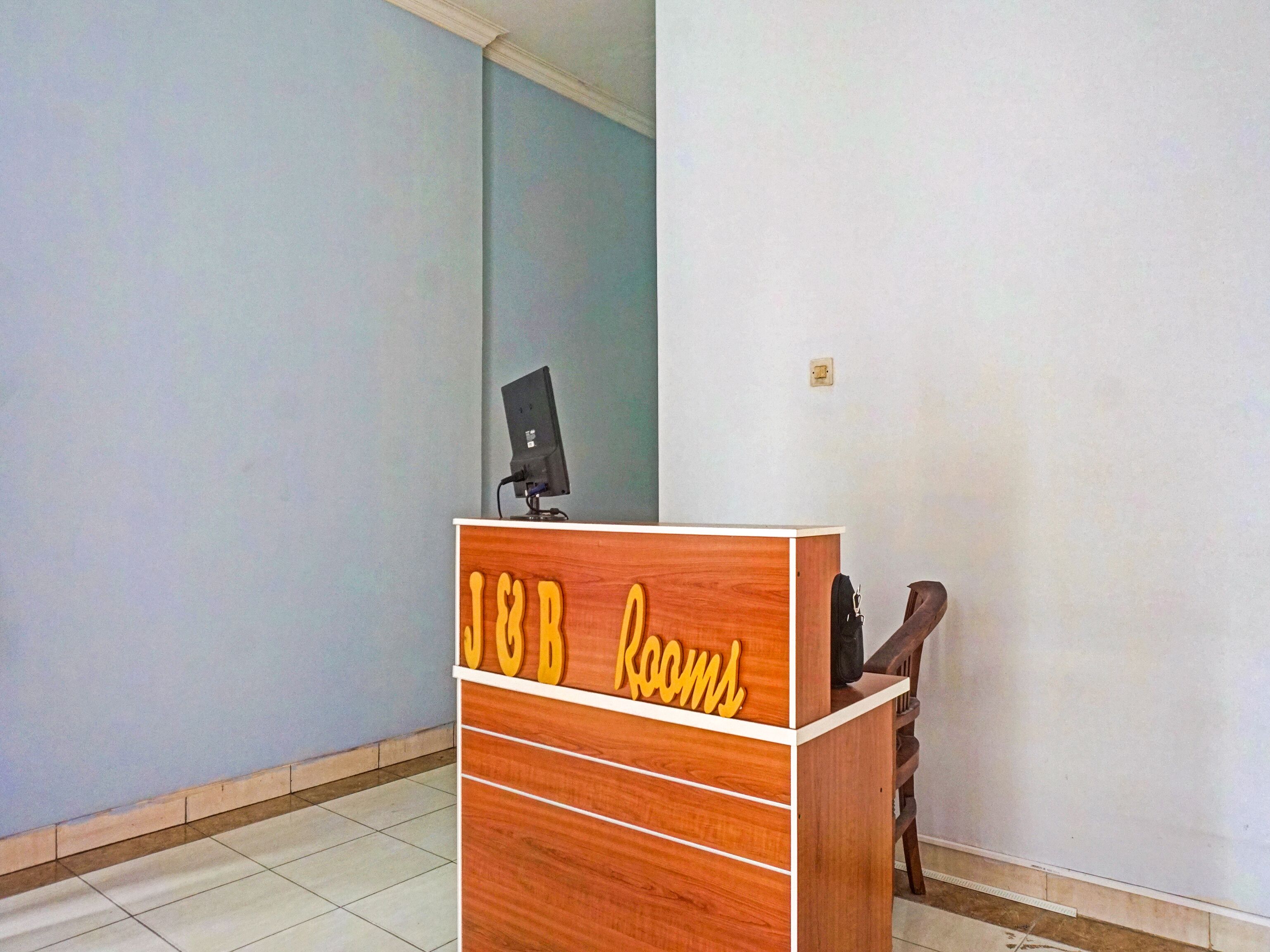 A wooden reception desk with a sign that reads "J&B Rooms" and a computer monitor on top.