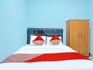A bed with a red and white bedspread, two red pillows, and a wooden wardrobe against a blue wall. - Hotel O J&b Rooms Tomang (Jakarta)