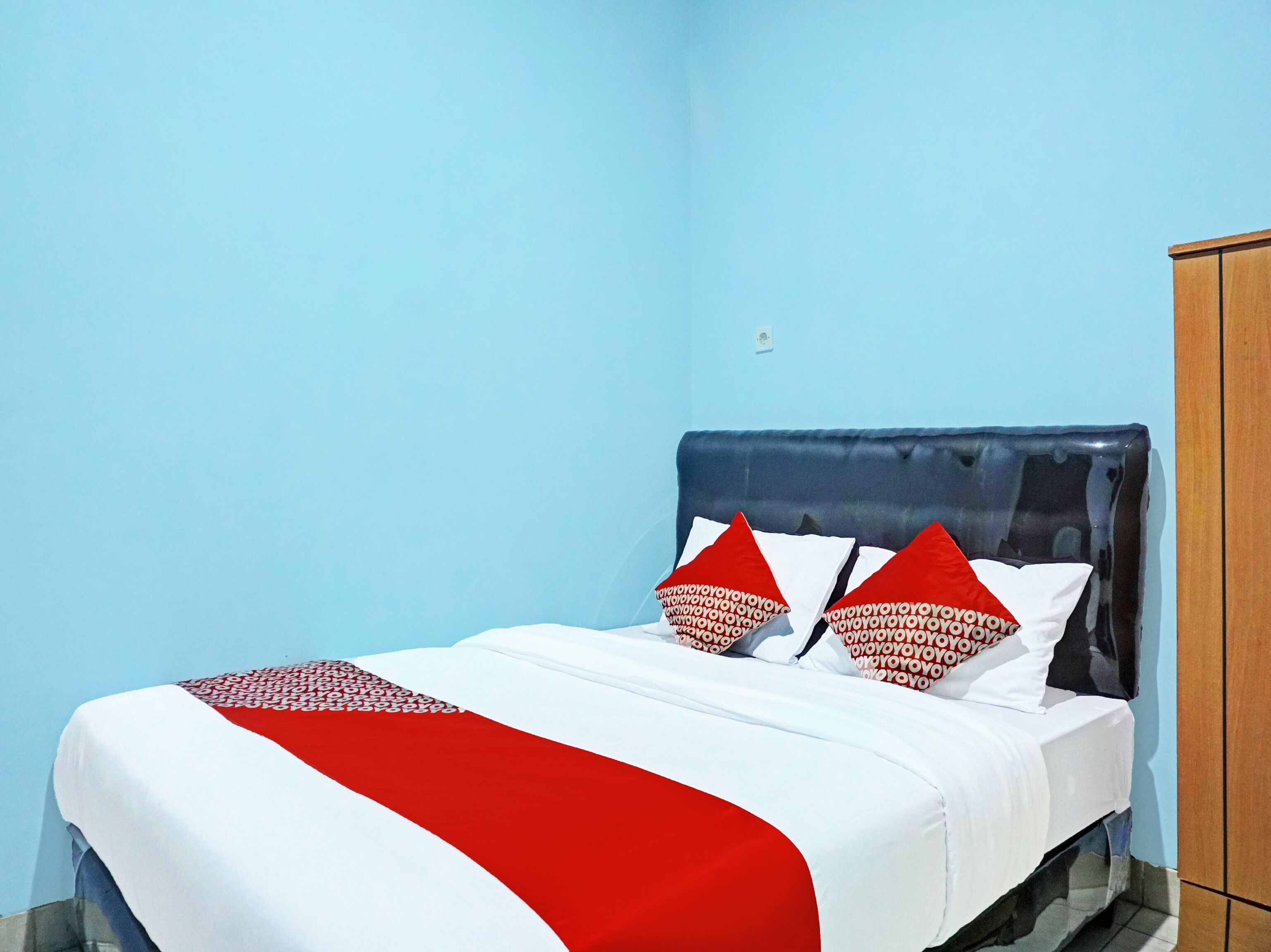 A bed with a red and white bedspread, two pillows with red and white patterns, and a dark headboard.