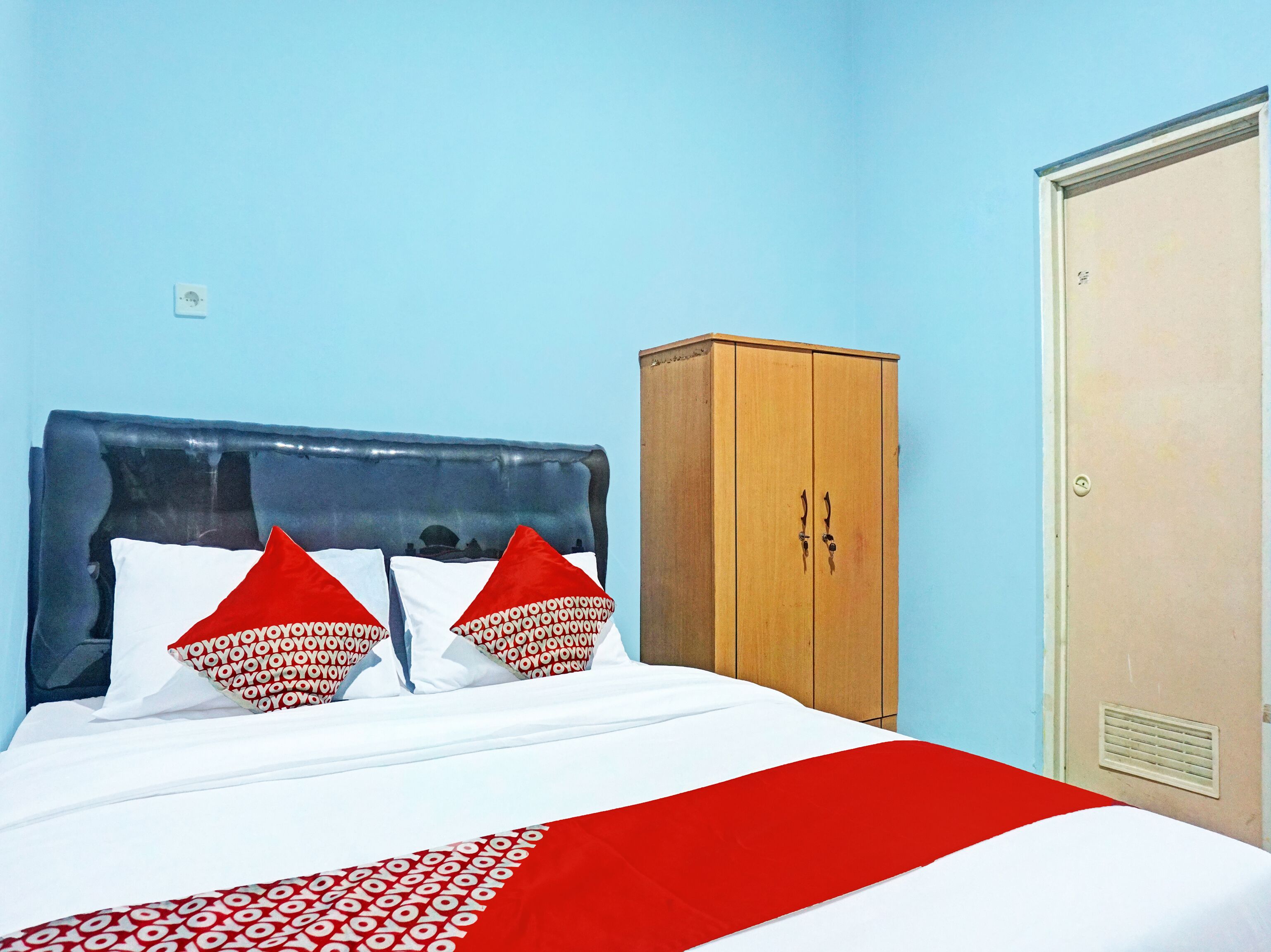 A bed with a blue headboard, two red pillows, and a white bedspread with a red and white pattern.