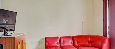 A room with a red leather sofa, a wooden cabinet with a television, and a plain wall.