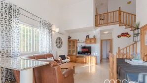 Ein geräumiges Wohnzimmer mit einem braunen Ledersofa, einem Fernseher, Holzschränken und einer Treppe.