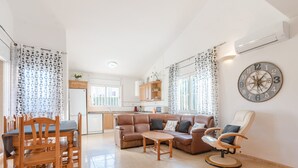 Ein geräumiger Wohnbereich mit einer Couch, Sesseln, einem Esstisch und einer Küche im Hintergrund.