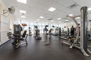 A gym with various exercise machines, large windows, and a ceiling fan.
