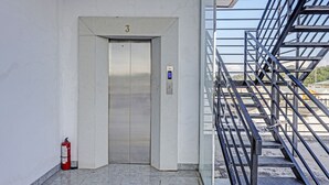 En elevator med digitalt display, brandslukker og trappe med metalgelændere.