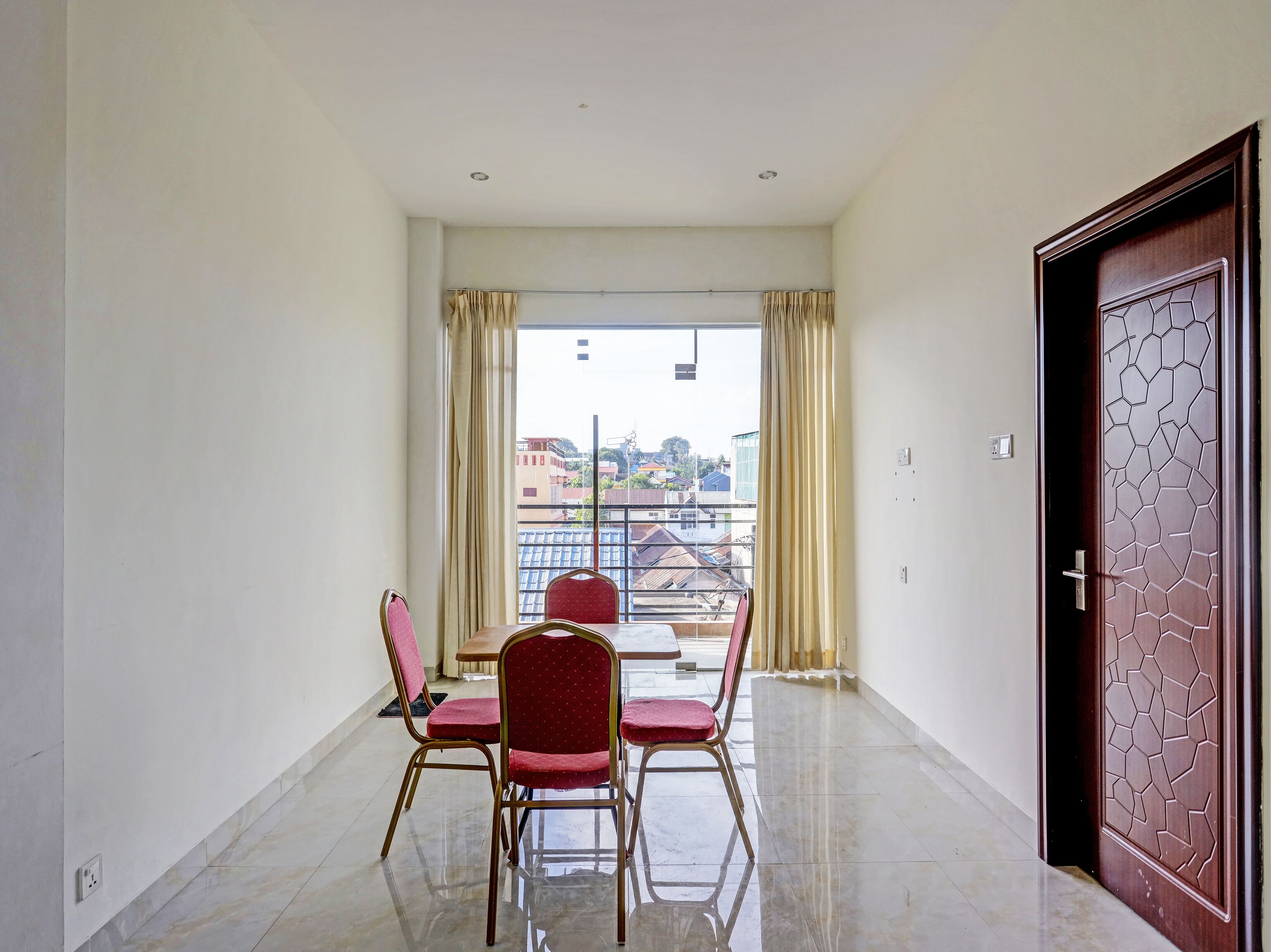 A balcony with a table and chairs, a view of buildings, and a door with a geometric pattern.