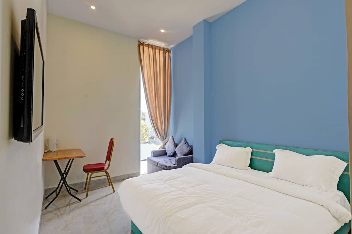 Ein Schlafzimmer mit Bett, einem an der Wand befestigten Fernseher, einem kleinen Tisch mit Stuhl und einem Fenster mit Vorhängen.