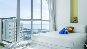 A hotel room with a large window, a bed with white bedding, two teddy bears, and a small shelf with a reindeer decoration.
